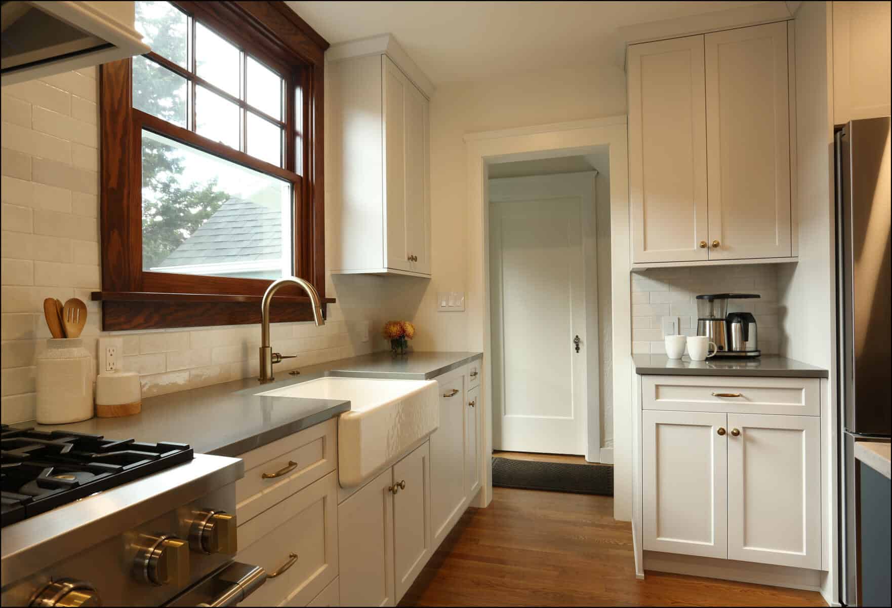 A modern kitchen with white cabinetry, stainless steel appliances, a farmhouse sink, and wooden flooring. A window above the sink allows natural light to enter the space. A modern kitchen with white cabinetry, stainless steel appliances, a farmhouse sink, and wooden flooring. A window above the sink allows natural light to enter the space.