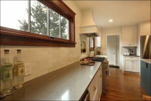A modern kitchen with white cabinetry, stainless steel appliances, a black countertop, and a large window. Two bottles and a cutting board with chopped vegetables are on the counter. A modern kitchen with white cabinetry, stainless steel appliances, a black countertop, and a large window. Two bottles and a cutting board with chopped vegetables are on the counter.