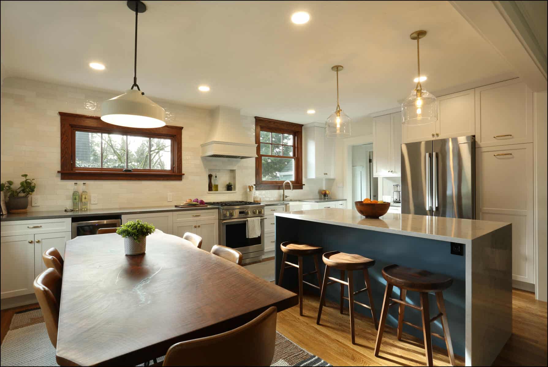 Modern kitchen with a wood dining table, island with marble countertop and stools, white cabinetry, stainless steel appliances, and pendant lights. Modern kitchen with a wood dining table, island with marble countertop and stools, white cabinetry, stainless steel appliances, and pendant lights.