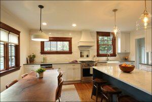 Modern kitchen with white cabinets, a marble countertop, pendant lights, a wooden dining table, and large windows. A bowl of fruit is on the island, and a plant is on the table. Modern kitchen with white cabinets, a marble countertop, pendant lights, a wooden dining table, and large windows. A bowl of fruit is on the island, and a plant is on the table.
