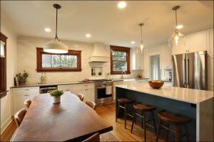 A modern kitchen with wooden floors, white cabinetry, stainless steel appliances, a large island with stools, and a dining table with a plant. Pendant lights hang over the island and dining area. A modern kitchen with wooden floors, white cabinetry, stainless steel appliances, a large island with stools, and a dining table with a plant. Pendant lights hang over the island and dining area.