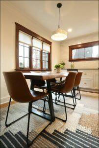 A dining room with a wooden table, four brown leather chairs, a ceiling pendant light, a potted plant on the table, and a window with white blinds in the background. A dining room with a wooden table, four brown leather chairs, a ceiling pendant light, a potted plant on the table, and a window with white blinds in the background.