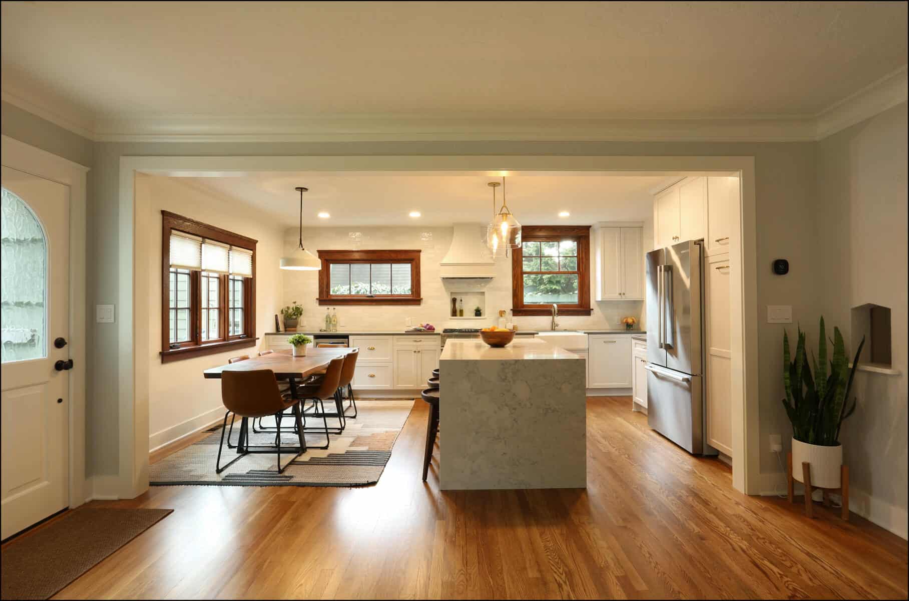 A modern kitchen with white cabinets, a large island, stainless steel appliances, and a wooden dining table with four chairs located near windows. The space features wooden floors and pendant lighting. A modern kitchen with white cabinets, a large island, stainless steel appliances, and a wooden dining table with four chairs located near windows. The space features wooden floors and pendant lighting.