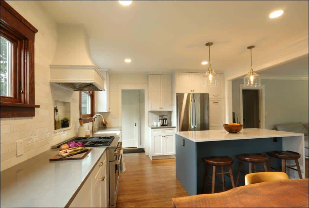 A modern kitchen with white cabinetry, stainless steel appliances, a central island with wooden stools, and a tiled backsplash. Hanging pendant lights illuminate the island. A modern kitchen with white cabinetry, stainless steel appliances, a central island with wooden stools, and a tiled backsplash. Hanging pendant lights illuminate the island.