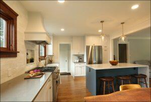 A modern kitchen with white cabinetry, stainless steel appliances, a central island with wooden stools, and a tiled backsplash. Hanging pendant lights illuminate the island. A modern kitchen with white cabinetry, stainless steel appliances, a central island with wooden stools, and a tiled backsplash. Hanging pendant lights illuminate the island.