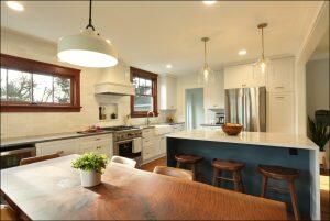 Modern kitchen with wooden dining table, potted plant centerpiece, stainless steel appliances, white cabinets, and island with bar stools and pendant lights. Modern kitchen with wooden dining table, potted plant centerpiece, stainless steel appliances, white cabinets, and island with bar stools and pendant lights.