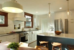 A modern kitchen with white cabinets, stainless steel appliances, an island with wooden stools, pendant lighting, and a bowl of fruit on the countertop. A small plant decorates the dining table. A modern kitchen with white cabinets, stainless steel appliances, an island with wooden stools, pendant lighting, and a bowl of fruit on the countertop. A small plant decorates the dining table.