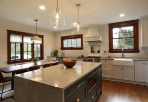 Modern kitchen with an island countertop, sink, and stove; a dining table is in the background near a window. Two pendant lights hang over the island. The space features white cabinets and wood accents. Modern kitchen with an island countertop, sink, and stove; a dining table is in the background near a window. Two pendant lights hang over the island. The space features white cabinets and wood accents.