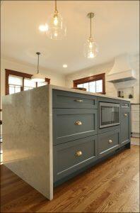 A modern kitchen with a large, marble-top island featuring teal cabinetry, brass handles, and built-in microwave. The room has hardwood floors, pendant lights, and natural light from surrounding windows. A modern kitchen with a large, marble-top island featuring teal cabinetry, brass handles, and built-in microwave. The room has hardwood floors, pendant lights, and natural light from surrounding windows.