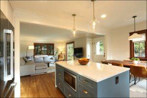 A modern open-concept kitchen with a large island and pendant lights overlooks a dining area and a living room with a sectional sofa and TV. A modern open-concept kitchen with a large island and pendant lights overlooks a dining area and a living room with a sectional sofa and TV.