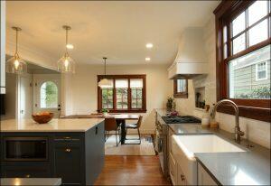 A modern kitchen with an island featuring a microwave and fruit bowl, stainless steel appliances, a sink, a stove, and seating area with a table and chairs near a window. Natural light illuminates the space. A modern kitchen with an island featuring a microwave and fruit bowl, stainless steel appliances, a sink, a stove, and seating area with a table and chairs near a window. Natural light illuminates the space.