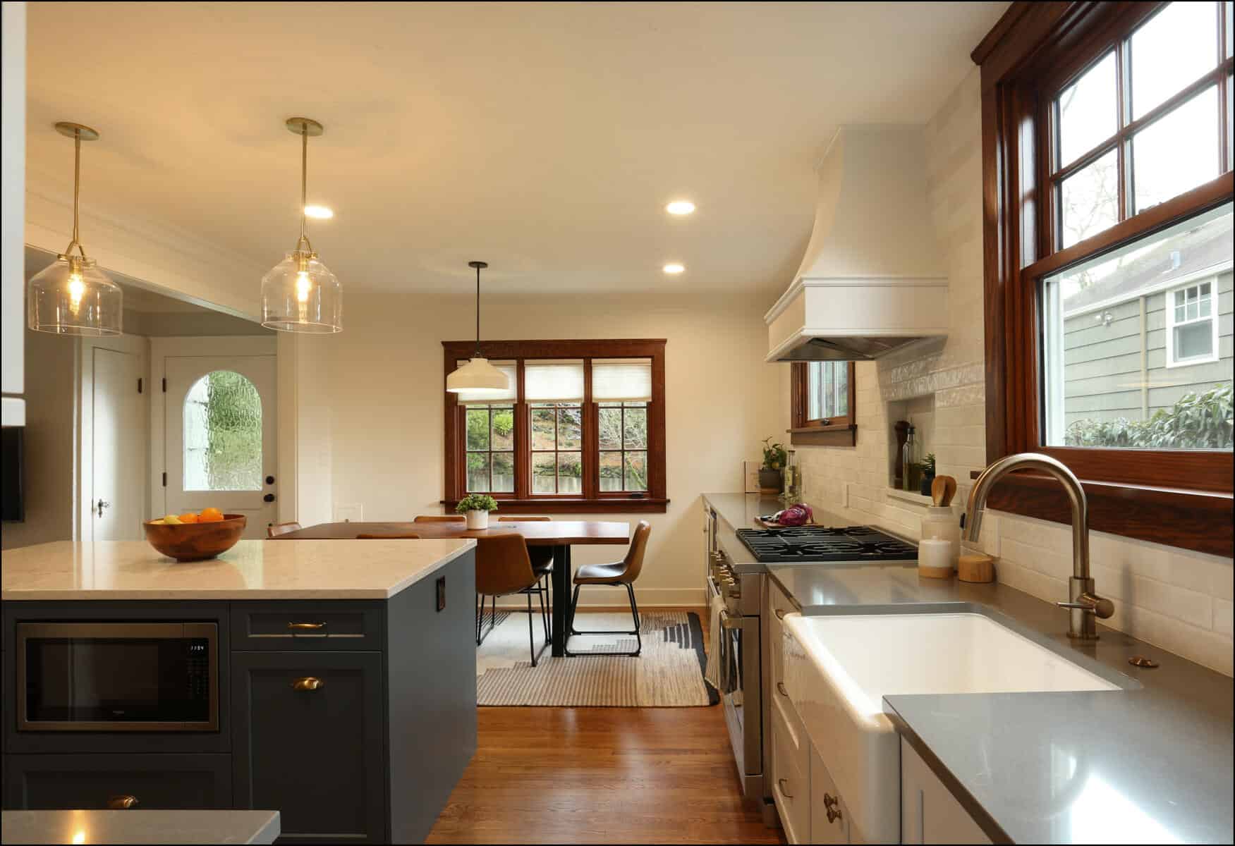 A modern kitchen with an island featuring a microwave and fruit bowl, stainless steel appliances, a sink, a stove, and seating area with a table and chairs near a window. Natural light illuminates the space. A modern kitchen with an island featuring a microwave and fruit bowl, stainless steel appliances, a sink, a stove, and seating area with a table and chairs near a window. Natural light illuminates the space.