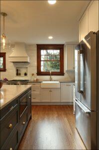 Modern kitchen with white cabinetry, stainless steel appliances, a central island with a marble countertop, and a farmhouse sink under a window. Hardwood floors and pendant lighting complete the setup. Modern kitchen with white cabinetry, stainless steel appliances, a central island with a marble countertop, and a farmhouse sink under a window. Hardwood floors and pendant lighting complete the setup.