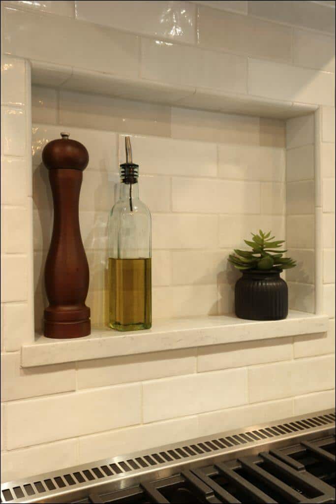 A kitchen nook with a pepper grinder, a bottle of olive oil, and a small potted succulent placed on a white tiled backsplash above a stove. A kitchen nook with a pepper grinder, a bottle of olive oil, and a small potted succulent placed on a white tiled backsplash above a stove.