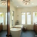 A modern bathroom, boasting a freestanding bathtub in the center, dual sinks, pendant lights, and frosted windows. This award-winning residential bathroom remodel exemplifies elegance and innovation, earning recognition with the 2024 NARI CotY Regional Award.