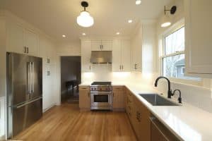 A modern, well-lit kitchen with stainless steel appliances, white cabinets, light wood flooring, black fixtures, and ample counter space designed by a top remodeling contractor in Portland.