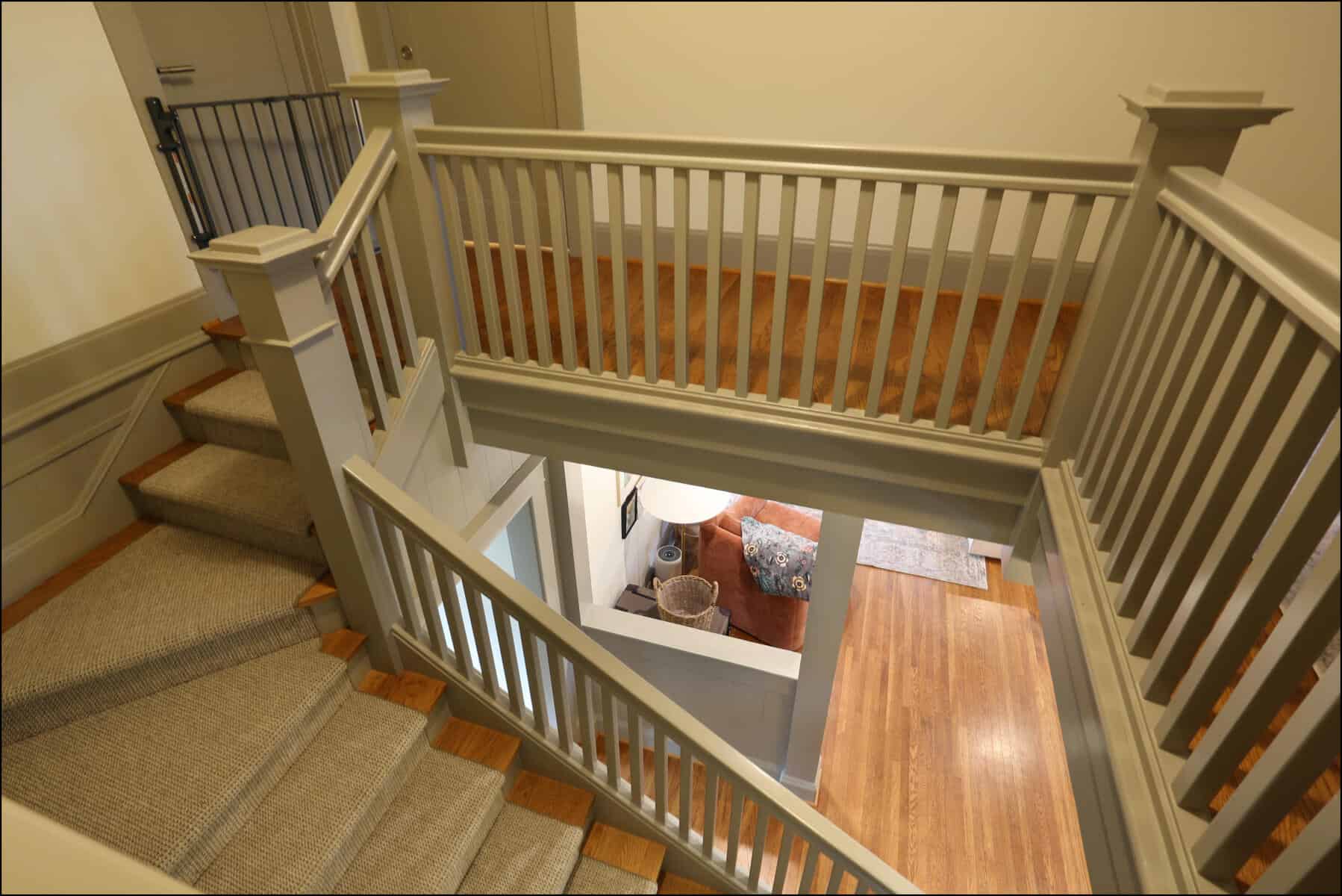 View of a staircase with wooden railings, beige carpet on the steps, and a glimpse of a room with hardwood flooring below. Staircase with gray railings leading to an open area, showcasing a whole house remodel by ReCraft Home Remodeling in Portland, Oregon.