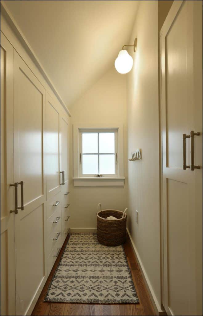 A narrow, well-lit hallway with built-in cabinets on the left, a small window at the end, a patterned rug on the wooden floor, and a wicker basket in the corner. A narrow, well-lit hallway with built-in cabinets on the left, a small window at the end, a patterned rug on the wooden floor, and a wicker basket in the corner.