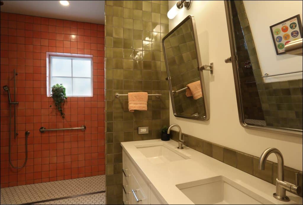 Bathroom with dual sinks, green tiled wall, two mirrors, and an adjacent shower area with orange tiles and a window. Bathroom with dual sinks, green tiled wall, two mirrors, and an adjacent shower area with orange tiles and a window.