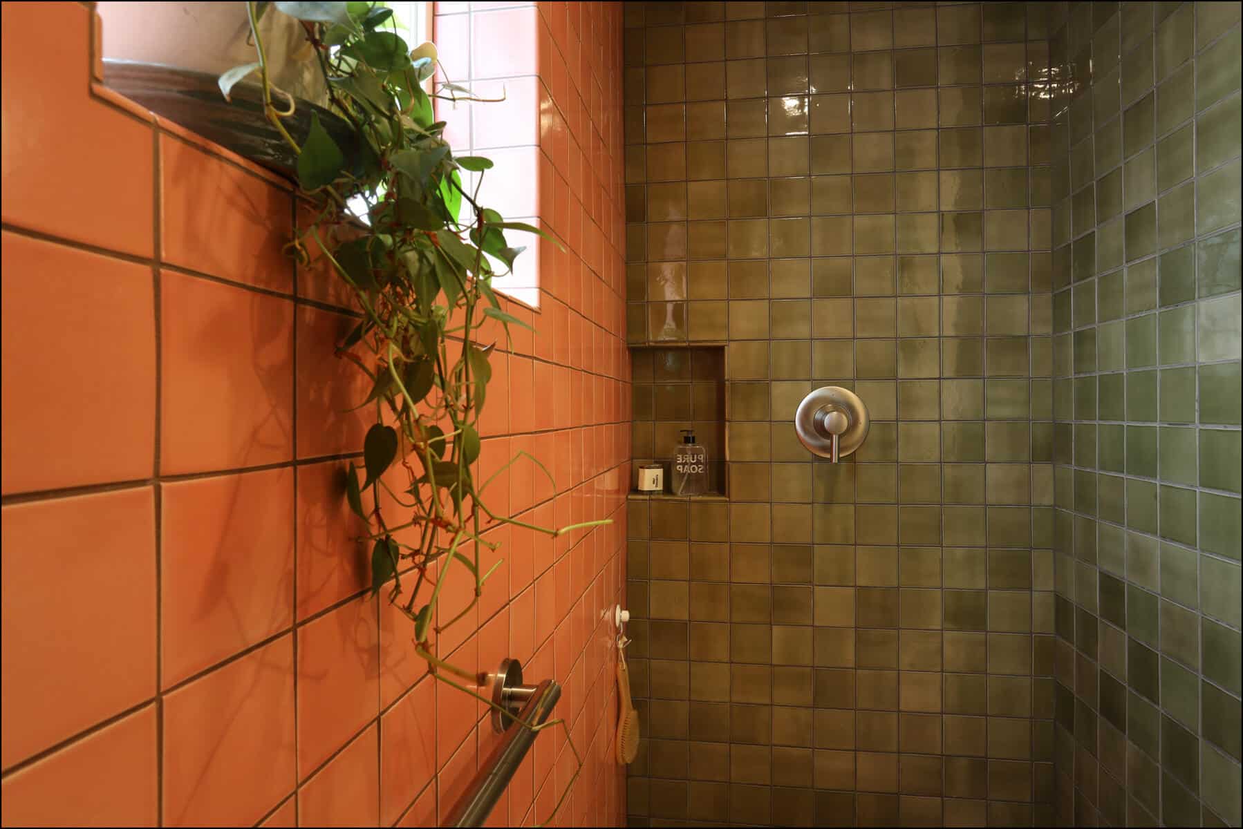 Shower area featuring a blend of orange and green tiled walls, with a wall-mounted shower fixture and a small window adorned with greenery, showcasing a modern and vibrant design suitable for whole house remodeling in Portland.
