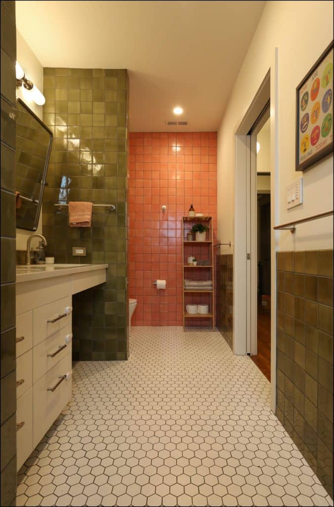 Bathroom with green and pink tiled walls, hexagonal floor tiles, a countertop with sink, mirror, and shelving unit. A framed picture hangs on the wall. Bathroom with green and pink tiled walls, hexagonal floor tiles, a countertop with sink, mirror, and shelving unit. A framed picture hangs on the wall.
