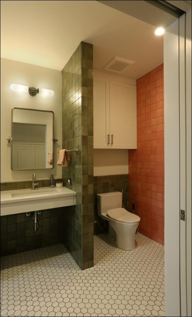 A bathroom with green and pink tiles, a sink with a mirror, and a toilet. The floor features hexagonal white tiles. A bathroom with green and pink tiles, a sink with a mirror, and a toilet. The floor features hexagonal white tiles.