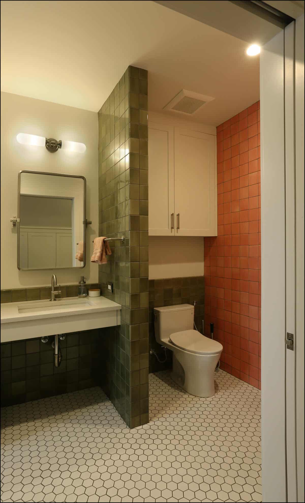 Modern bathroom interior featuring green and orange tiled walls, a white sink with a mirror, and a toilet, showcasing ReCraft Home Remodeling's design expertise in Portland.