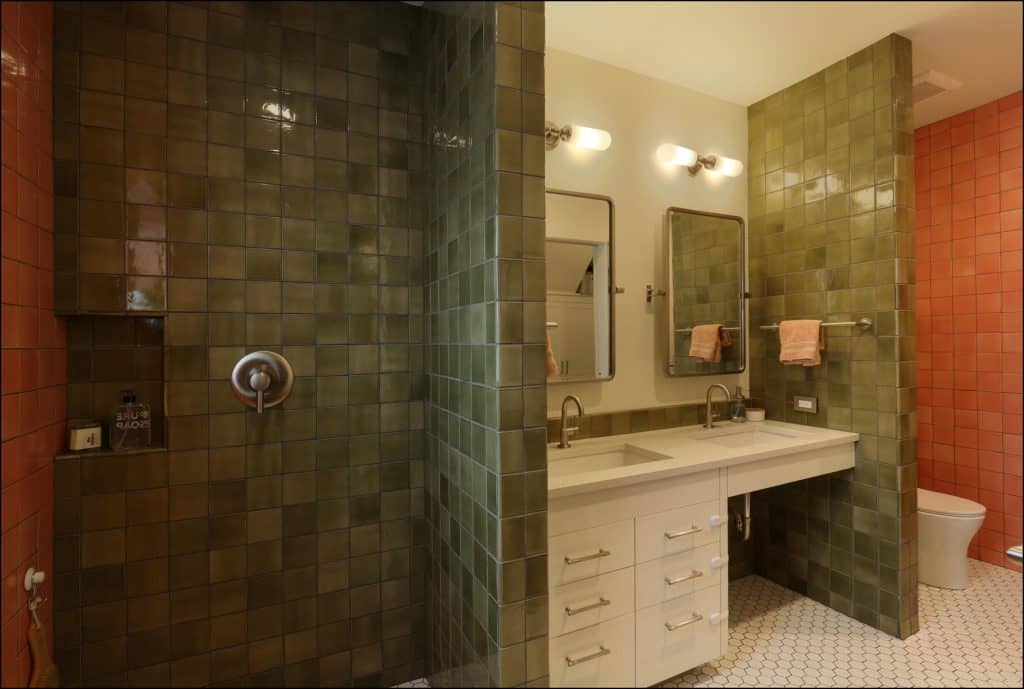 Bathroom with green and red tiled walls, two sinks with mirrors, a shower area, and a toilet. Bathroom with green and red tiled walls, two sinks with mirrors, a shower area, and a toilet.