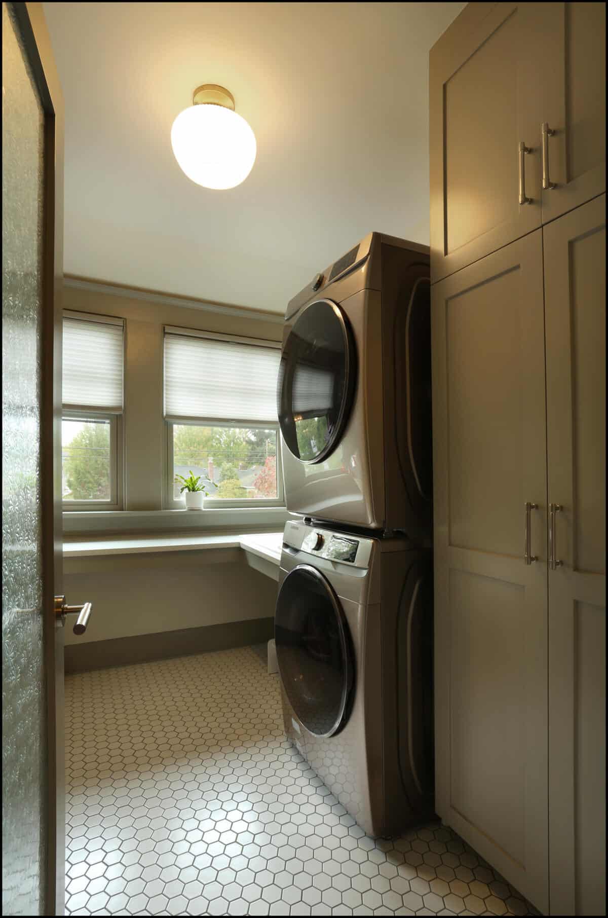 Laundry room featuring stacked washer and dryer units, modern cabinetry, hexagonal tile flooring, and natural light from windows, showcasing ReCraft Home Remodeling's design capabilities in Portland, Oregon.