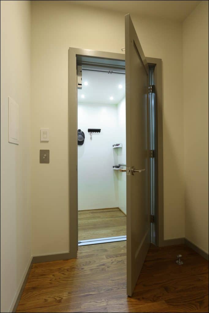 An open grey door leads to a well-lit, small closet with wooden flooring. Shelves and hooks are visible inside. An open grey door leads to a well-lit, small closet with wooden flooring. Shelves and hooks are visible inside.