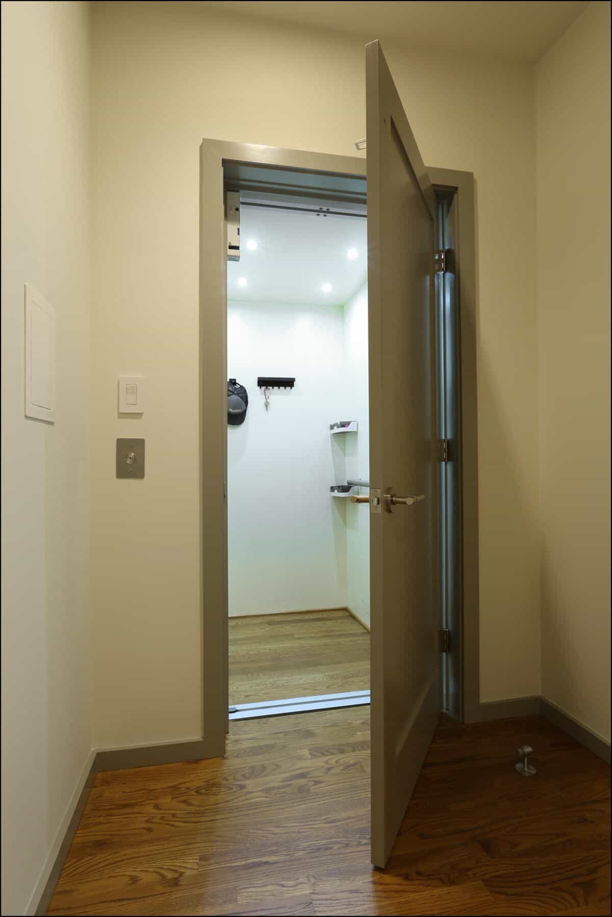 An open grey door leads to a well-lit, small closet with wooden flooring. Shelves and hooks are visible inside. Interior view of a modern doorway leading to a well-lit room with wooden flooring, showcasing a clean and minimalist design, relevant to ReCraft Home Remodeling's whole house remodeling projects in Portland.