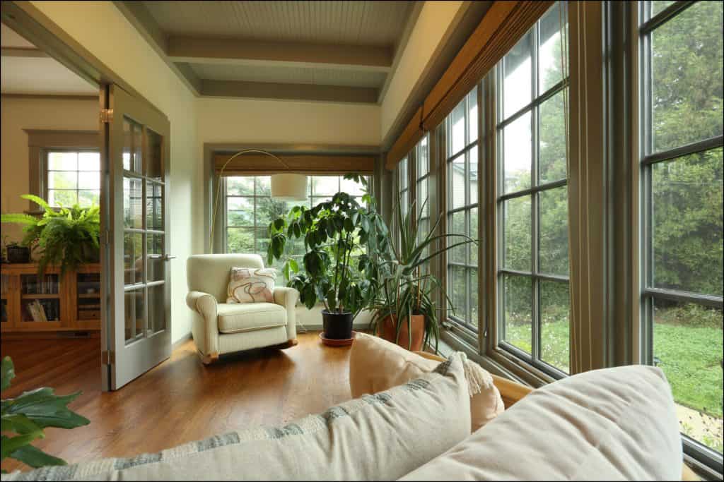A cozy sunroom with large windows, an armchair, potted plants, and wooden floors overlooking a garden. A cozy sunroom with large windows, an armchair, potted plants, and wooden floors overlooking a garden.