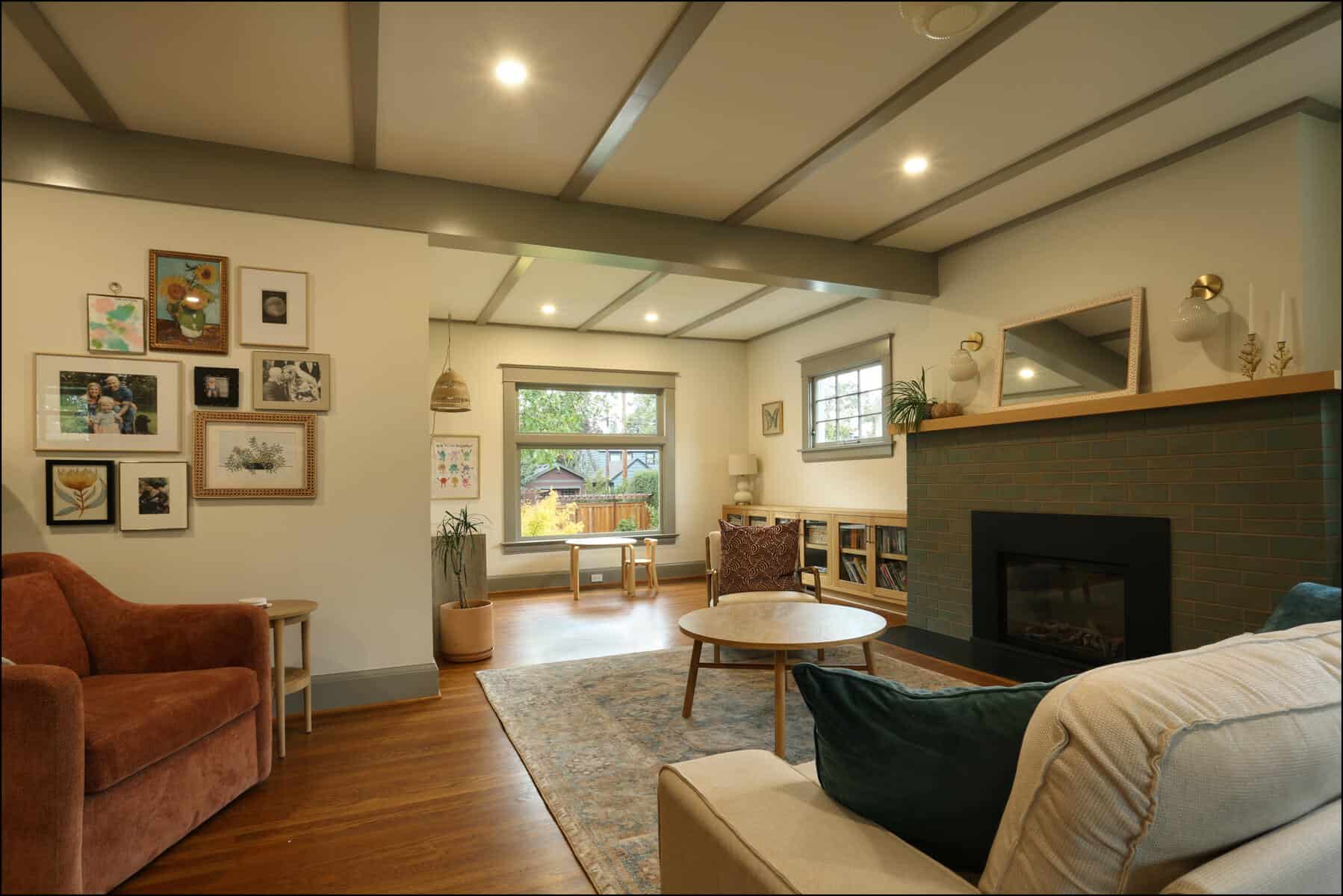 Cozy living room with a fireplace, round coffee table, and a mix of chairs. Walls display framed art, and a large window overlooks a garden. Soft lighting enhances the warm atmosphere. Cozy living room featuring a modern design with a fireplace, framed artwork on the walls, a round coffee table, and comfortable seating, showcasing ReCraft Home Remodeling's whole house remodeling expertise in Portland.