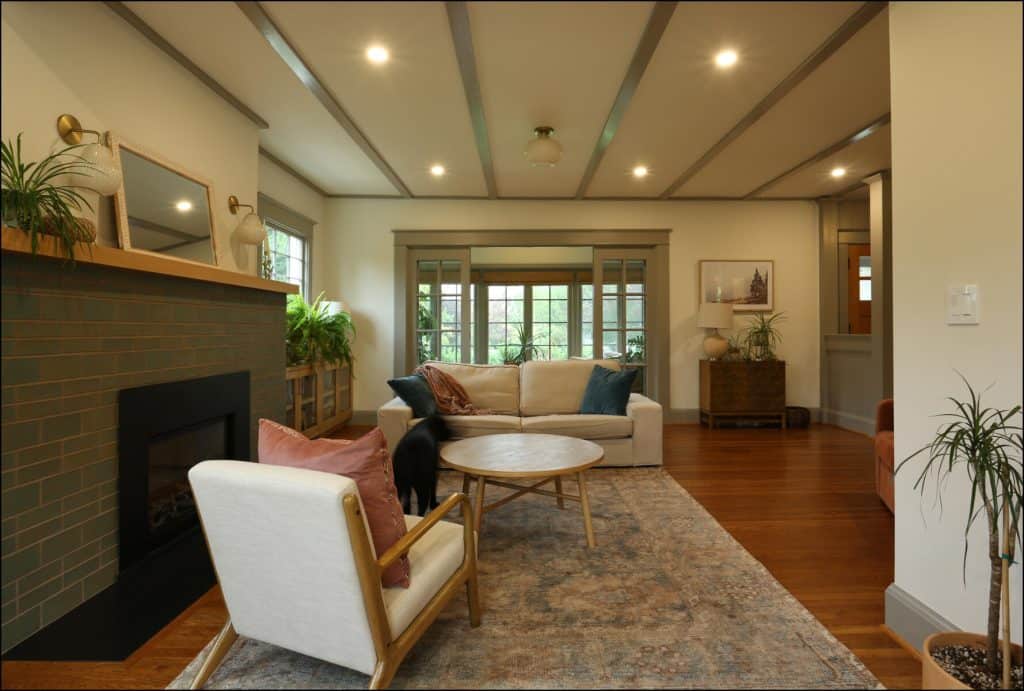 A cozy living room with a fireplace, beige armchair, white sofa, round wooden coffee table, and potted plants. Warm lighting and wooden flooring complete the inviting atmosphere. A cozy living room with a fireplace, beige armchair, white sofa, round wooden coffee table, and potted plants. Warm lighting and wooden flooring complete the inviting atmosphere.