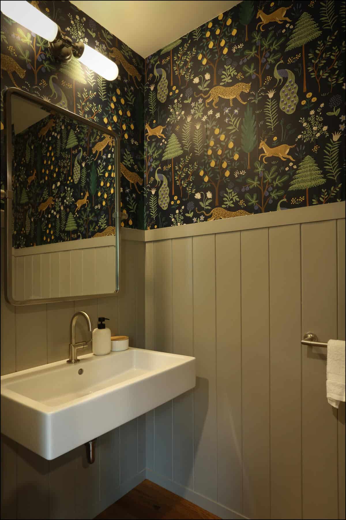 Small bathroom with a wall-mounted sink, decorative wallpaper with forest animals, and a rectangular mirror. Modern bathroom design featuring a wall-mounted sink, large mirror, and decorative wallpaper with woodland motifs, showcasing ReCraft Home Remodeling's interior design capabilities in whole house remodels.