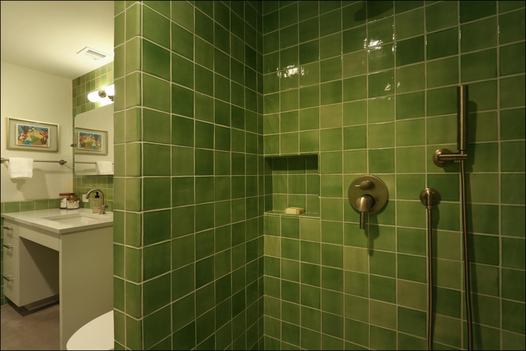 Bathroom with green tiled shower, bronze fixtures, and a soap niche; vanity with sink, mirror, and wall lights visible in the background. Shower area featuring vibrant green tile walls, modern fixtures, and a glimpse of a bathroom vanity, showcasing ReCraft Home Remodeling's design style in whole house renovations.
