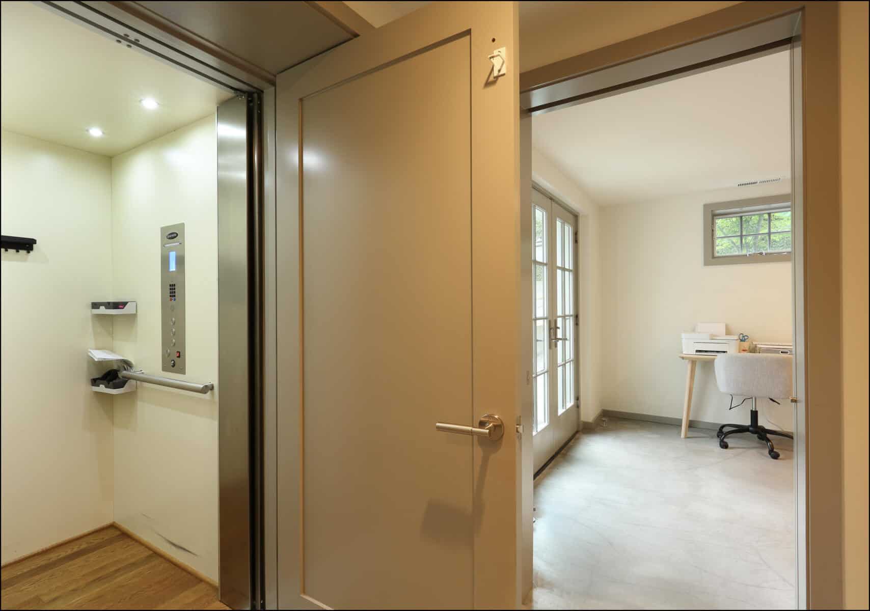 View of an open residential elevator next to a room with a desk and chair, illuminated by natural light from a window. Interior view of a modern hallway leading to a bright room with a desk, showcasing the quality of ReCraft Home Remodeling's whole house remodel projects in Portland, Oregon.