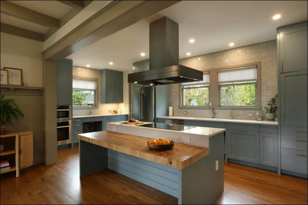 Modern kitchen with wooden floors, teal cabinets, and a central island with a wooden countertop. Two windows provide natural light. A bowl of oranges sits on the island. Modern kitchen with wooden floors, teal cabinets, and a central island with a wooden countertop. Two windows provide natural light. A bowl of oranges sits on the island.