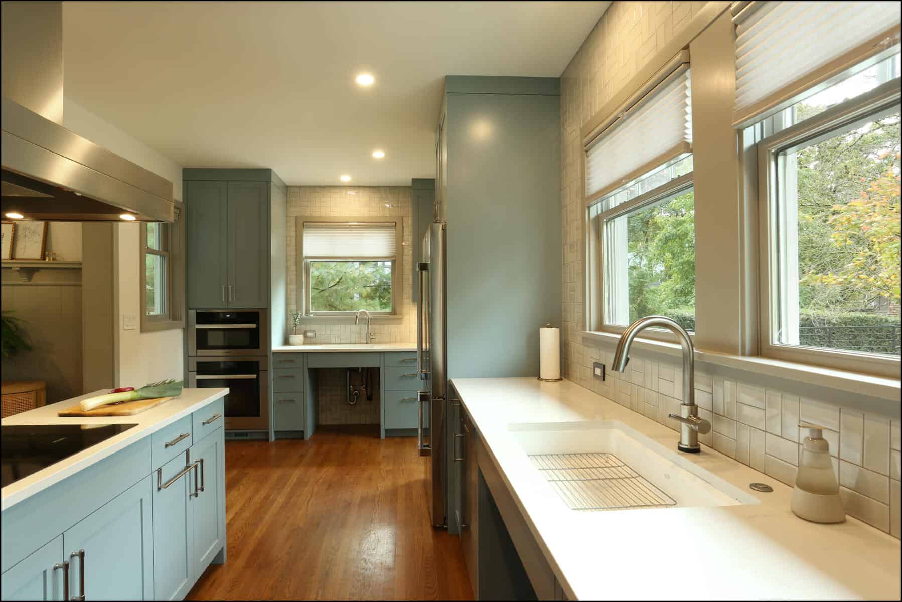 Bright kitchen with blue cabinets, white countertops, stainless steel appliances, and wooden floors. Large windows let in natural light. Bright kitchen with blue cabinets, white countertops, stainless steel appliances, and wooden floors. Large windows let in natural light.