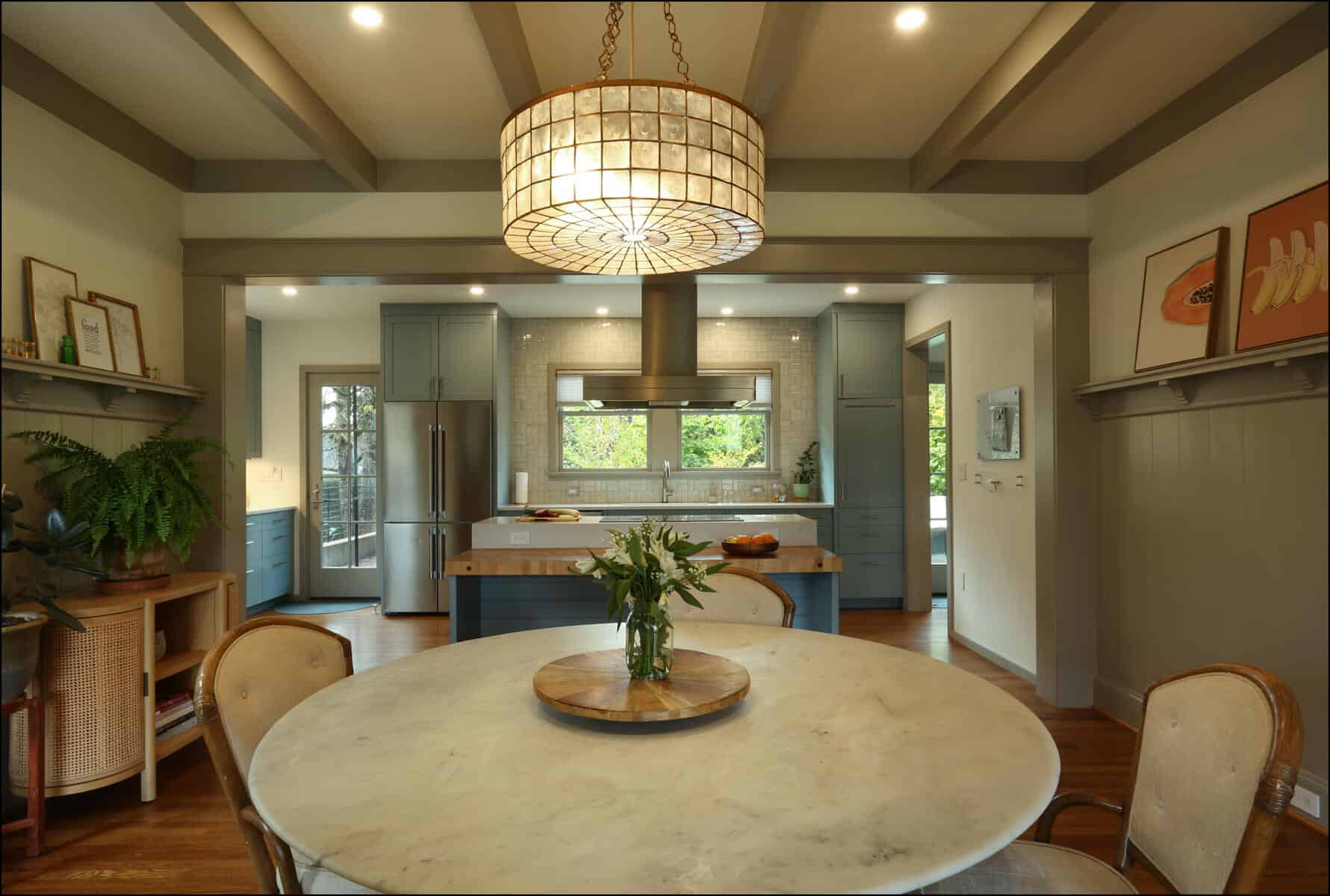 Spacious kitchen with a round marble dining table, beige chairs, a large ceiling light, and blue cabinets. The room features wood flooring and modern decor. Spacious kitchen with a round marble dining table, beige chairs, a large ceiling light, and blue cabinets. The room features wood flooring and modern decor.