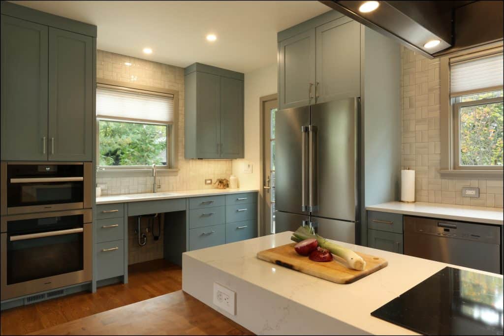 Modern kitchen with blue cabinets, stainless steel appliances, and a cutting board with vegetables on an island counter. Large windows provide natural light. Modern kitchen with blue cabinets, stainless steel appliances, and a cutting board with vegetables on an island counter. Large windows provide natural light.
