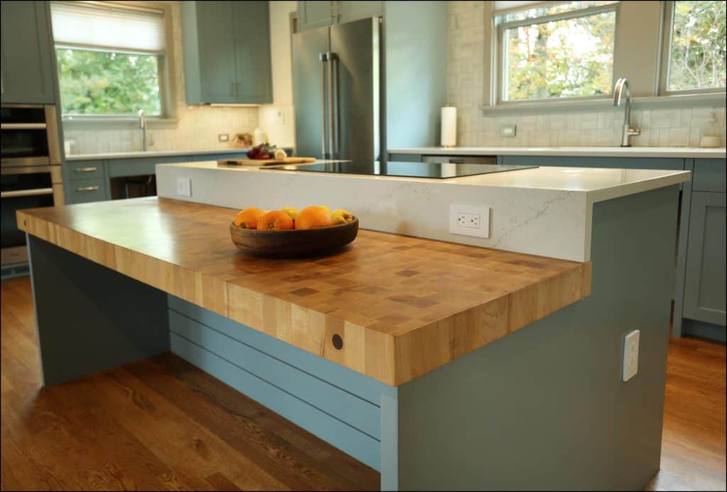 Modern kitchen with a wooden island countertop. A bowl of oranges sits on the counter. Stainless steel appliances and large windows are visible in the background. Modern kitchen with a wooden island countertop. A bowl of oranges sits on the counter. Stainless steel appliances and large windows are visible in the background.