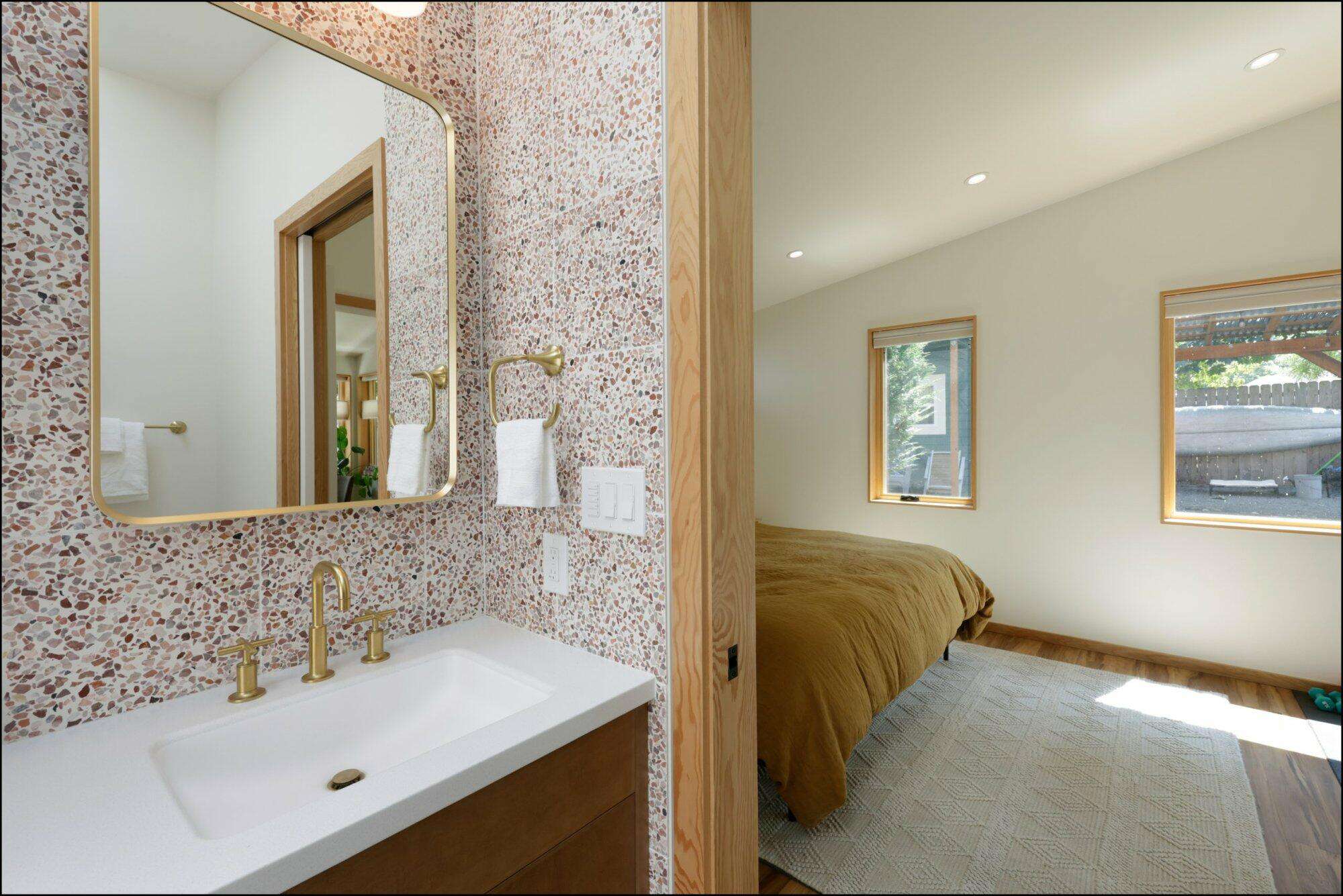 Modern bathroom design featuring a stylish sink with gold fixtures, textured wall tiles, and a view into a cozy bedroom with natural light and warm tones, showcasing ReCraft Home Remodeling's craftsmanship in Portland renovations.