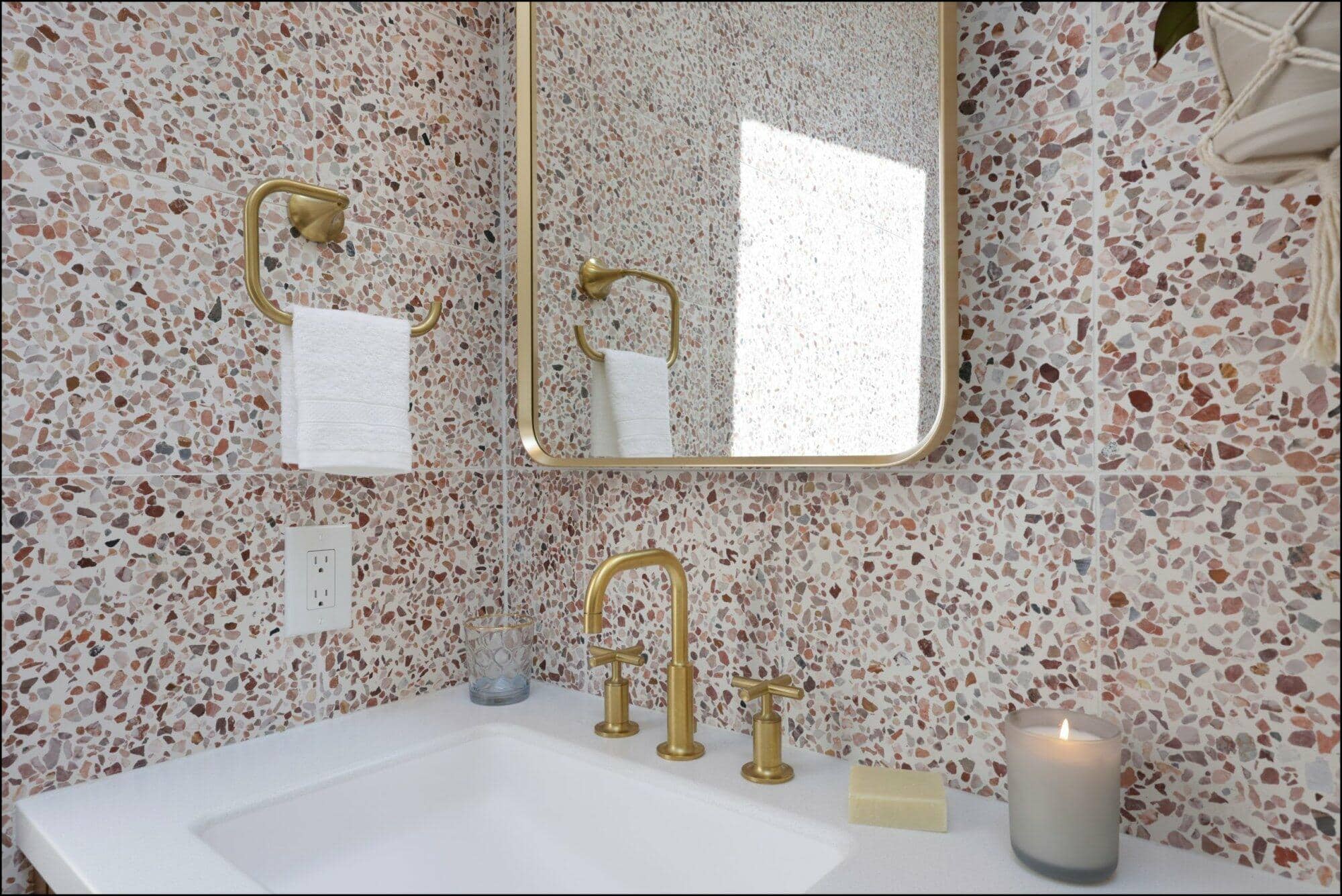 Bathroom sink area featuring a modern gold faucet, a rectangular mirror, and a textured terrazzo wall, complemented by a lit candle and decorative elements, showcasing ReCraft's bathroom remodeling design in Portland.