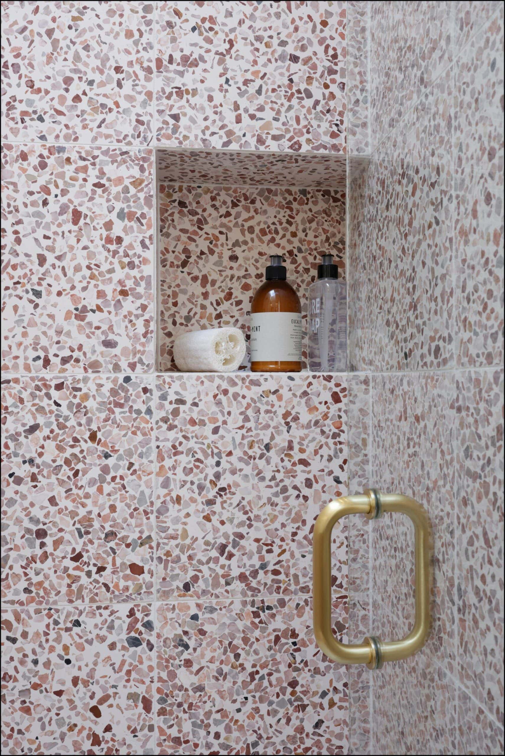 Bathroom niche with toiletries in a textured terrazzo wall, featuring a gold handle, showcasing modern design elements from ReCraft Home Remodeling in Portland, Oregon.