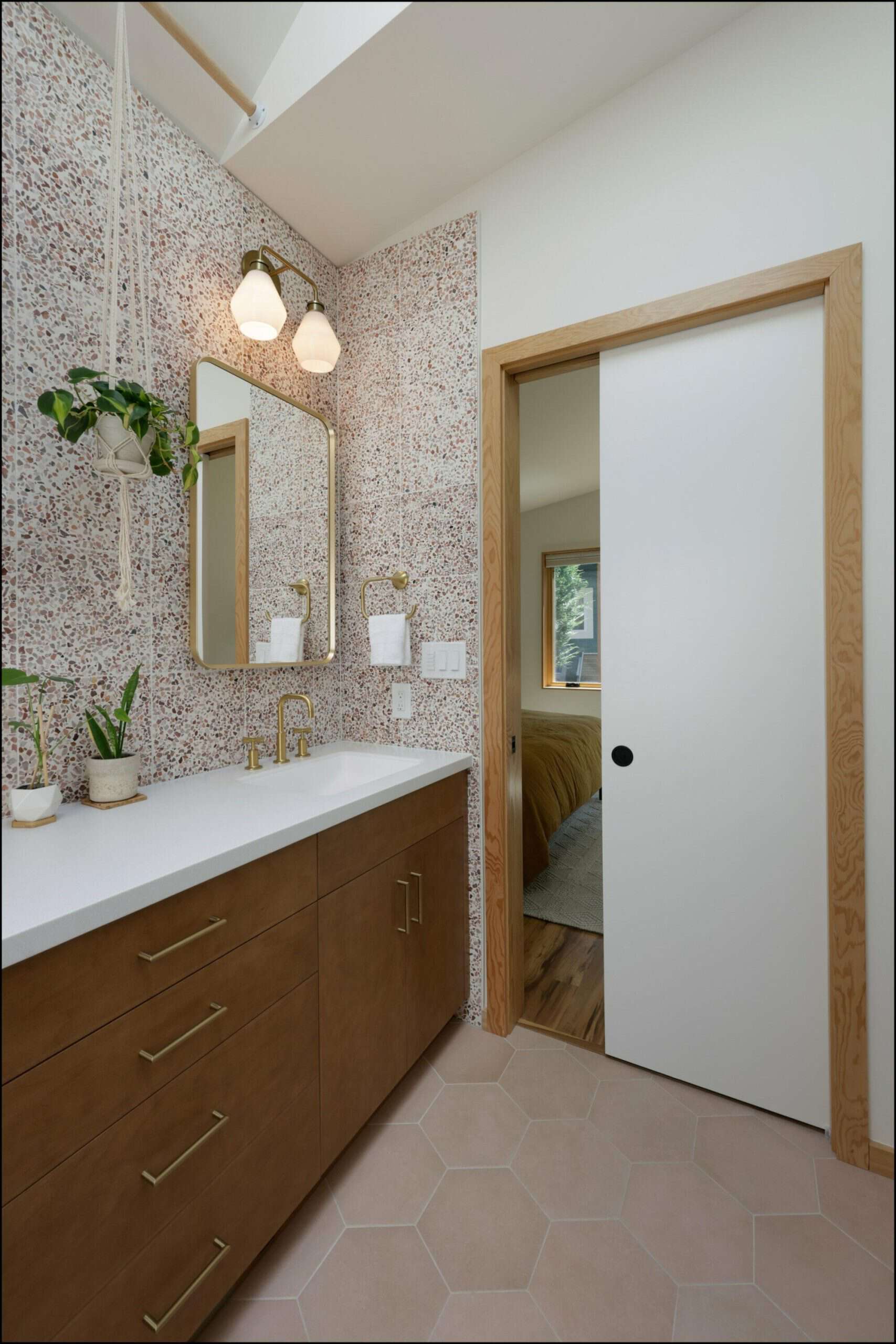 Modern bathroom interior featuring a pocket door, sleek wooden cabinetry, hexagonal tile flooring, and decorative wall plants, showcasing ReCraft Home Remodeling's design expertise in Portland bathroom renovations.