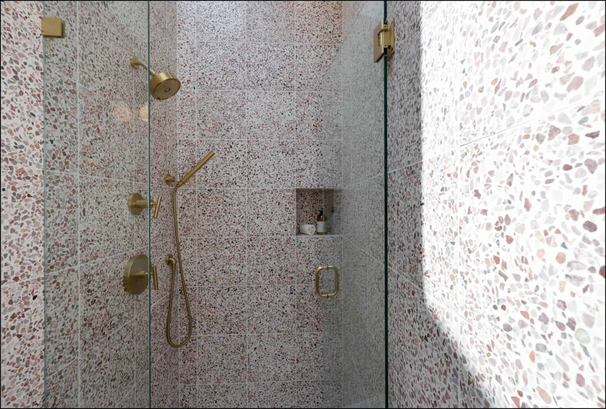 A modern shower features terrazzo tile walls, gold fixtures, and a glass door. A built-in niche holds toiletries.
