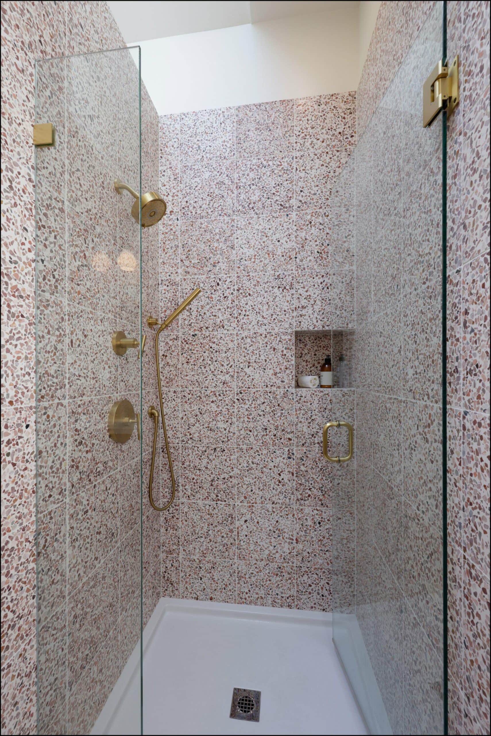 Modern bathroom shower with glass enclosure, featuring textured stone walls, gold fixtures, and a built-in niche for toiletries, showcasing ReCraft Home Remodeling's design expertise in Portland bathroom renovations.