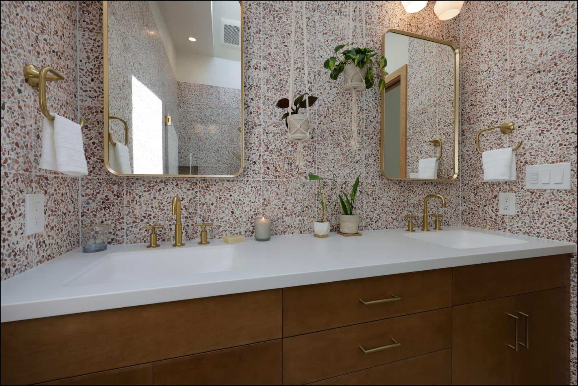 Bathroom with a double sink vanity, gold fixtures, large rectangular mirrors, hanging plants, and a terrazzo wall.