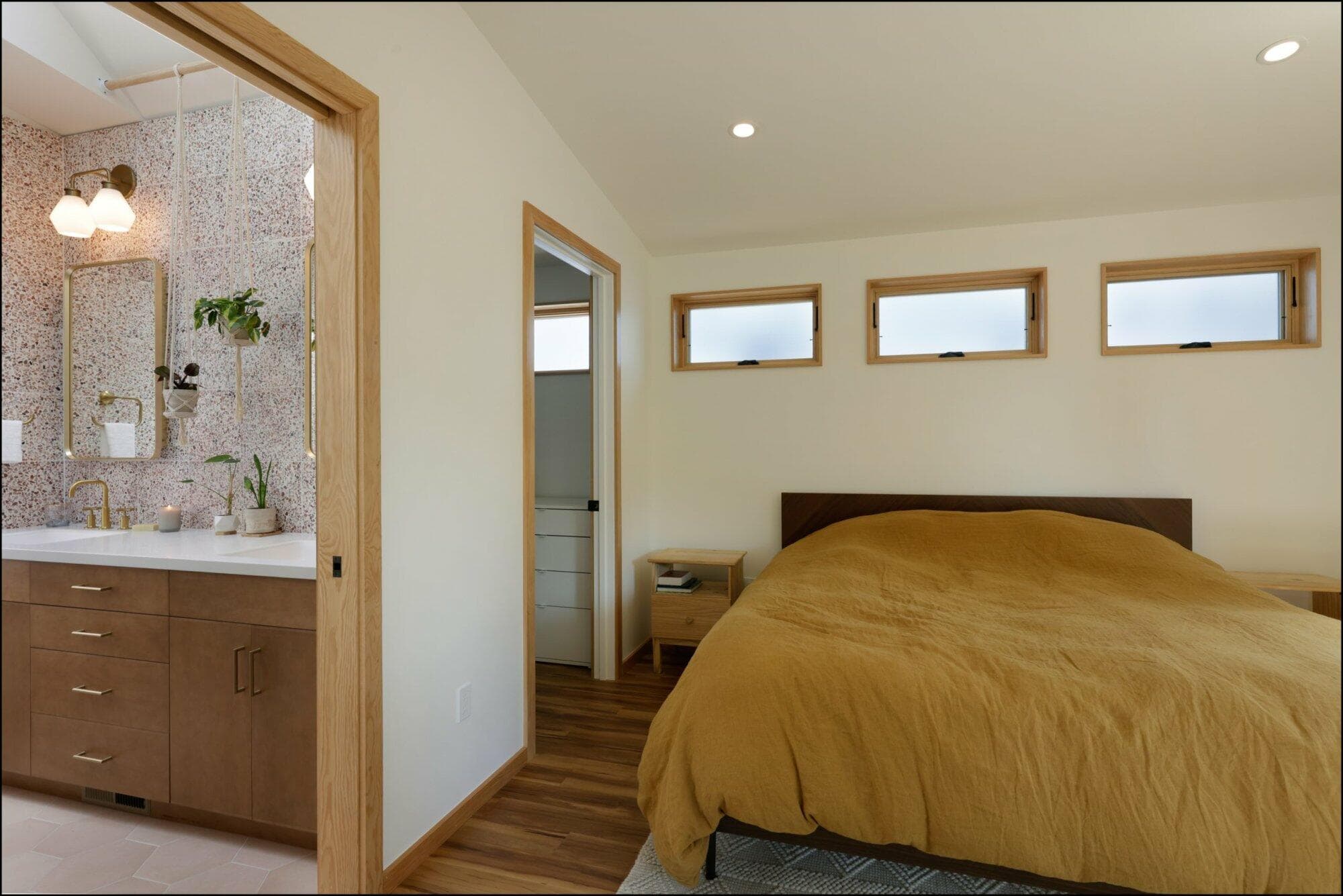 Bedroom interior featuring a cozy yellow bedspread, wooden accents, and an entrance to a stylish bathroom vanity area with modern fixtures, showcasing ReCraft Home Remodeling's design aesthetic in Portland.